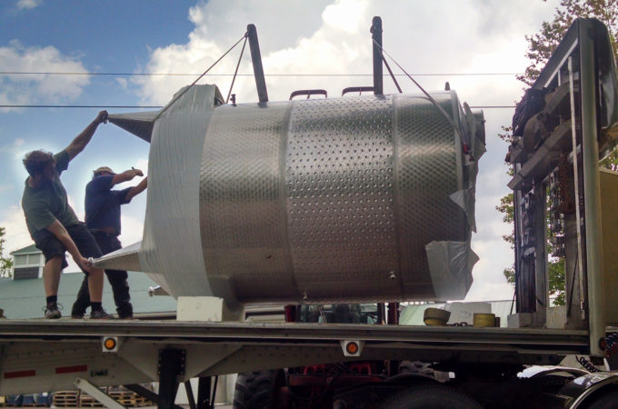 two men guide a large wine tank off a truck