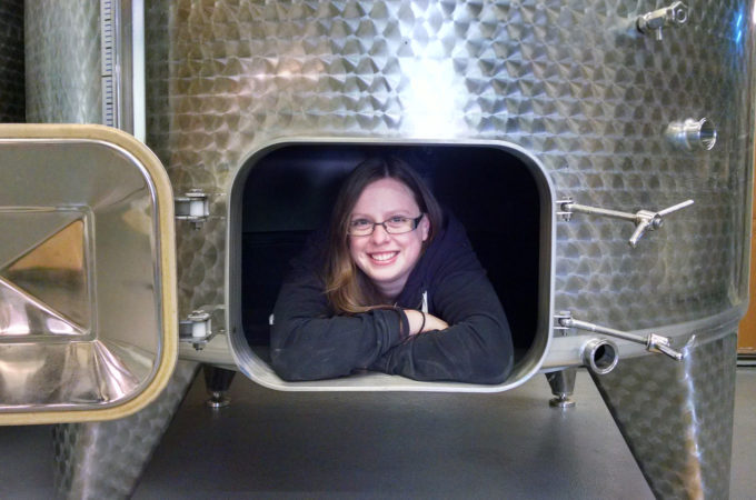young woman peaking out the door of a wine tank