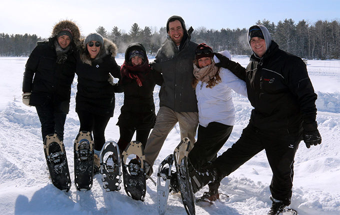 six smiling people in winter clothes wearing snowshoes