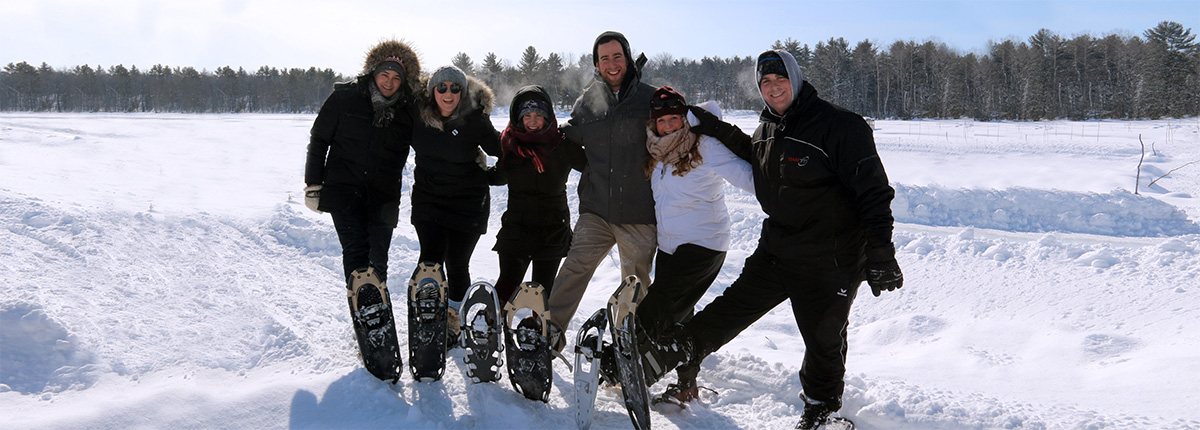 six smiling people in winter clothes wearing snowshoes