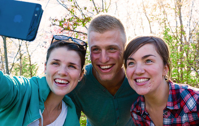 two girls and a guy taking a selfie in the woods