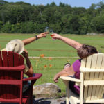 couple sitting on muskoka chairs overlooking old marsh reaching out to touch wine glasses