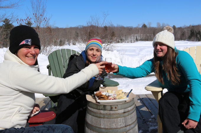 three girls touching glasses sitting outside on Muskoka chairs in winter