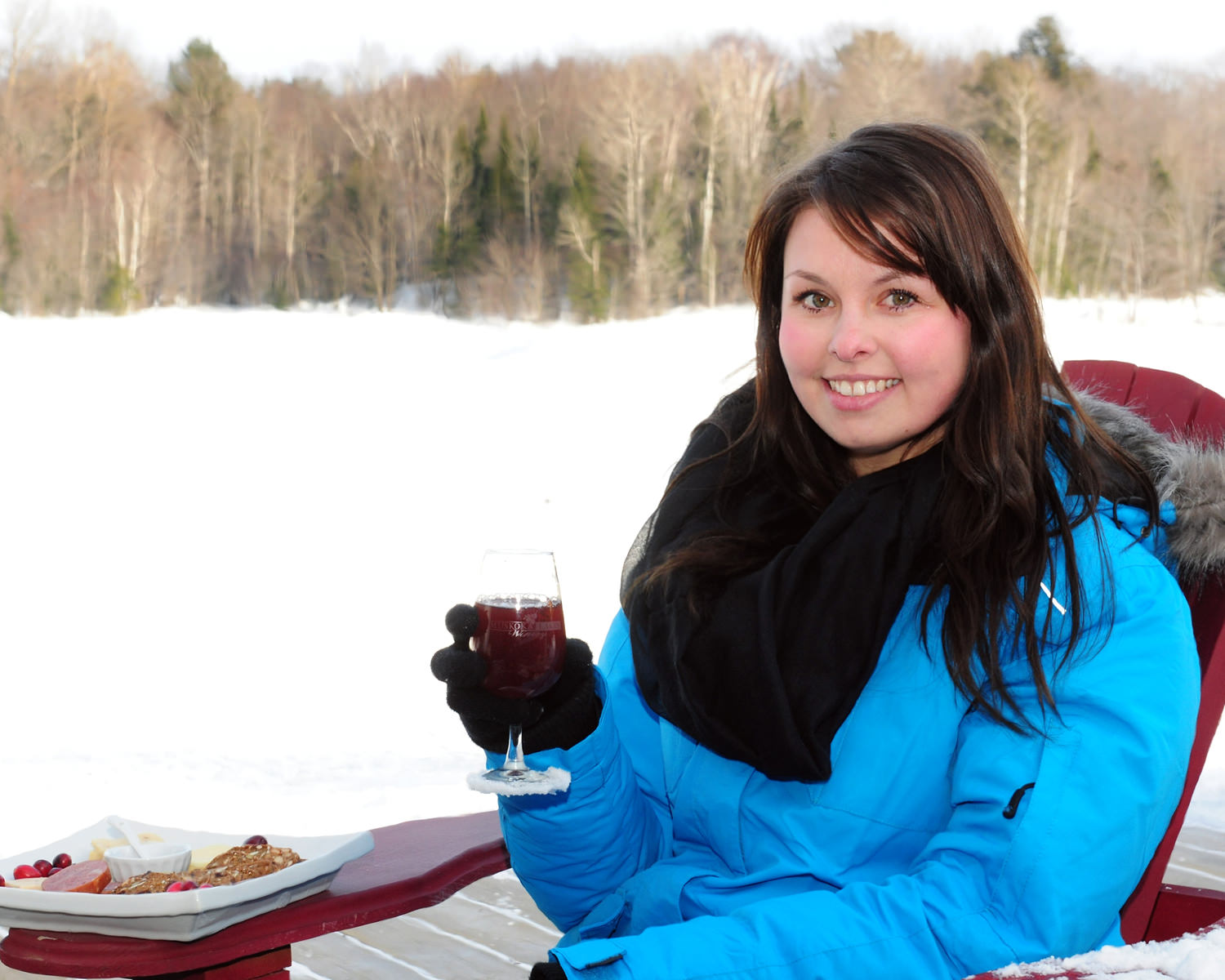 girl holding a glass of wine sitting outside on a muskoka chair with a cheese plate in winter