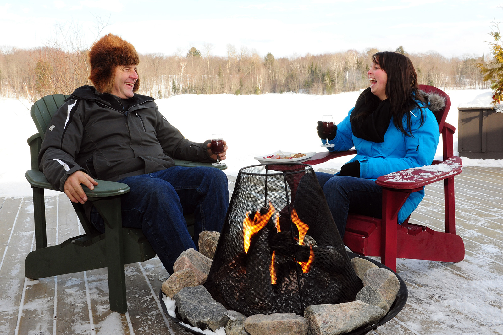 couple laughing and enjoying wine on an outdoor patio in front of a fire in winter time