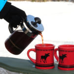 hot mulled wine being poured into two red moose mugs with snow in the background