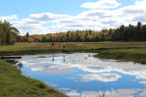 couple hiking along a dike with a blue pond reflecting clouds in the foreground