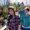 two girls and a guy laughing and crossing a bridge in the woods