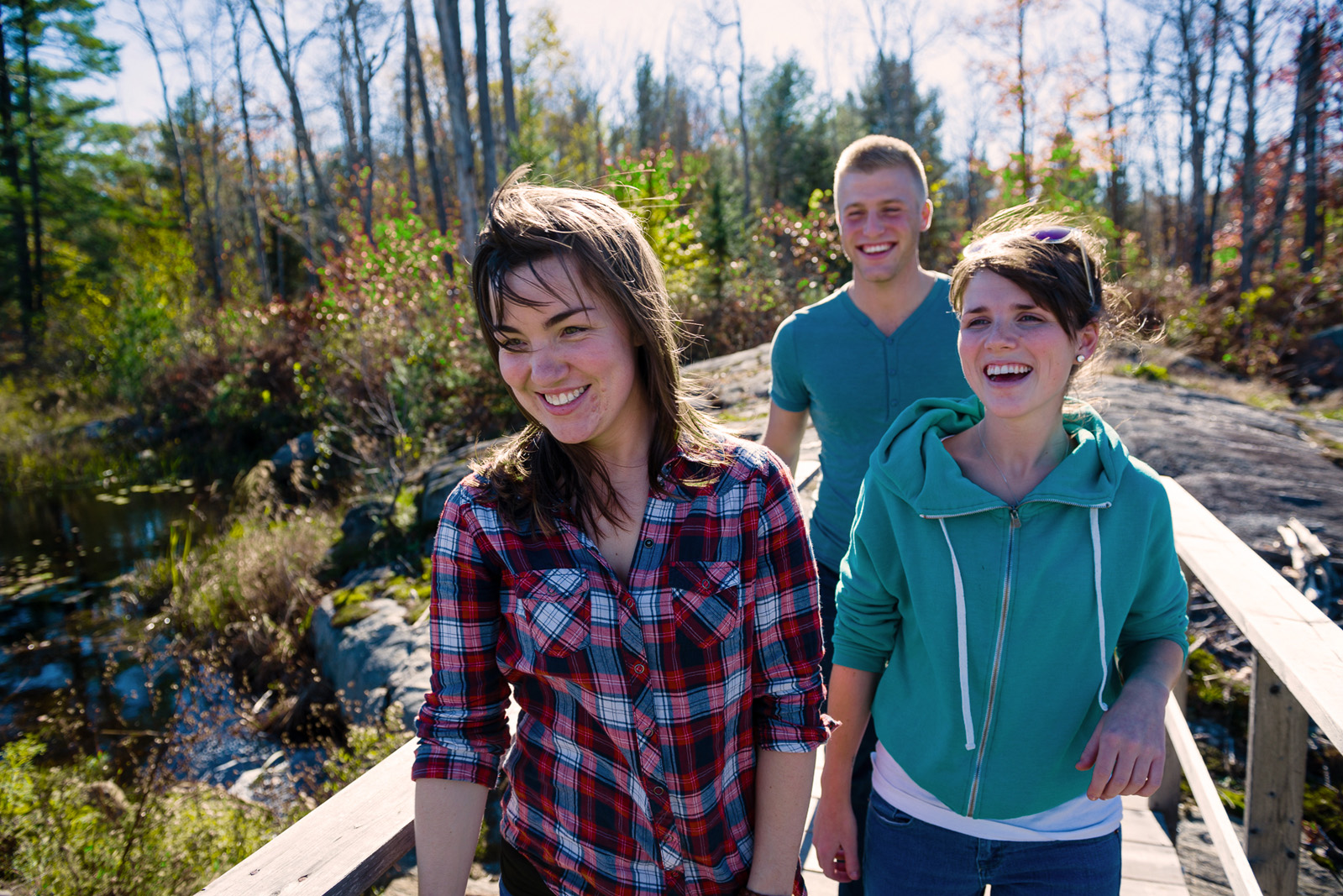 two girls and a guy laughing and crossing a bridge in the woods