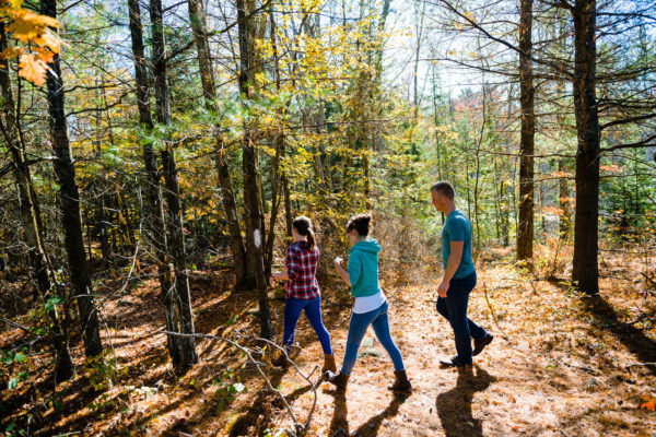two girls and a guy hiking in the woods in autumn