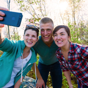 two girls and a guy posing for a selfie in the woods