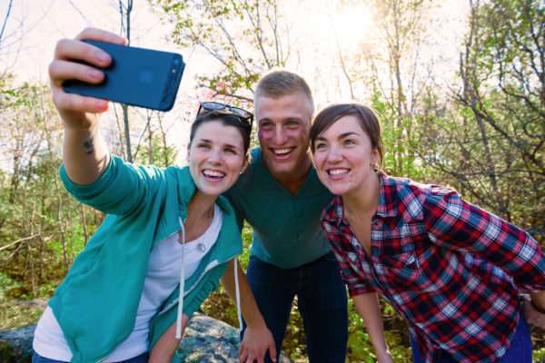two girls and a guy posing for a selfie in the woods