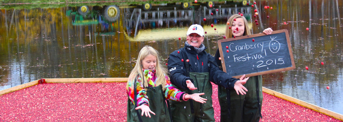 family tossing cranberries standing in floating cranberries with wagon in background