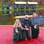 family tossing cranberries standing in floating cranberries with wagon in background