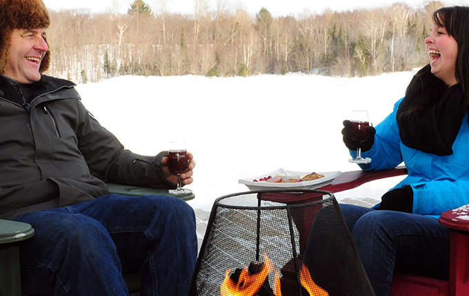 couple laughing enjoying wine & cheese by an outdoor fire in winter