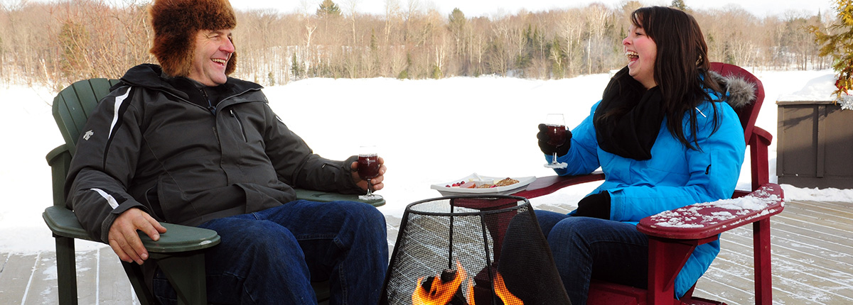 couple laughing enjoying wine & cheese by an outdoor fire in winter