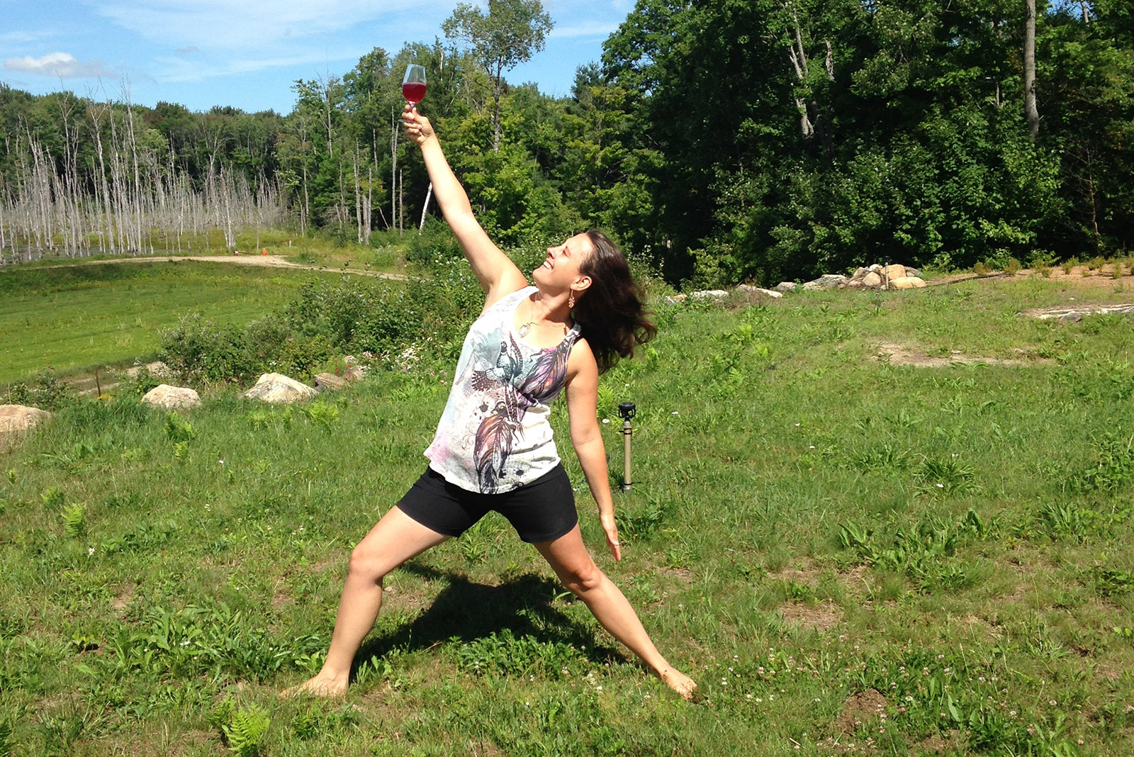 woman outdoors in yoga pose holding up glass of wine
