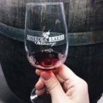 glass with Muskoka Lakes Winery logo in front of an oak barrel