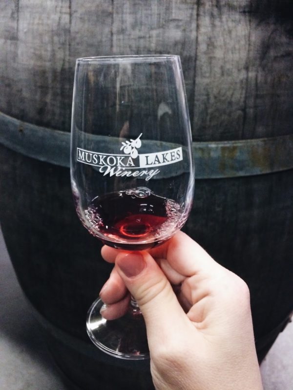 glass with Muskoka Lakes Winery logo in front of an oak barrel
