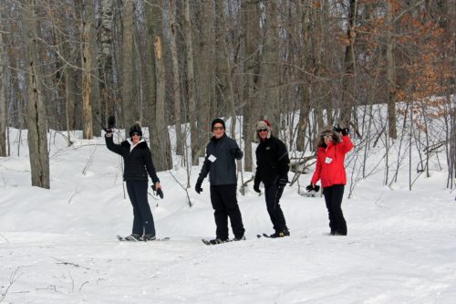 four people snowshoeing and waving