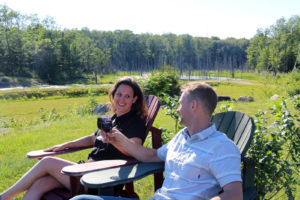 couple in Muskoka chairs toasting with wine glasses on top of blueberry hill