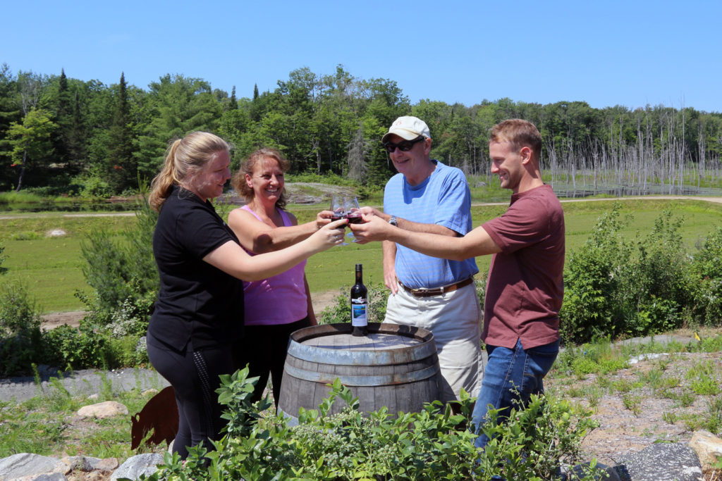 four smiling people around a wine barrel toasting with blueberry wine on top of blueberry hill