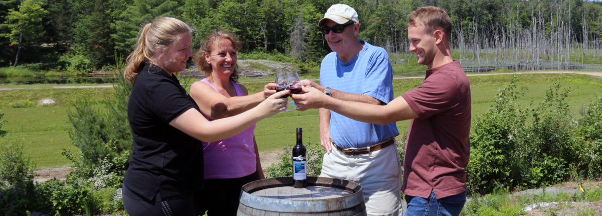 four smiling people around a wine barrel toasting with blueberry wine on top of blueberry hill