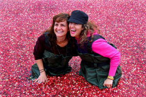 two women laughing as they kneel in cranberries