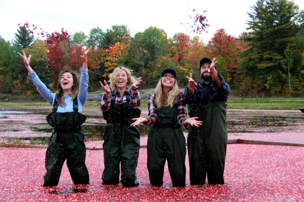 three women and a man laughing and throwing cranberries in the air