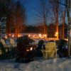 fire pit surrounded by muskoka chairs with ice trail in the background lit with torches for night skating