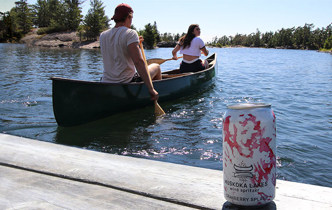 couple paddling canoe with can of spritzer on the dock behind them