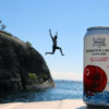 man jumping off cliff with can of cliff jump cranberry cider in the foreground