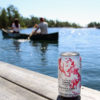 couple paddling a canoe with cranberry splash wine spritzer in the foreground on the dock
