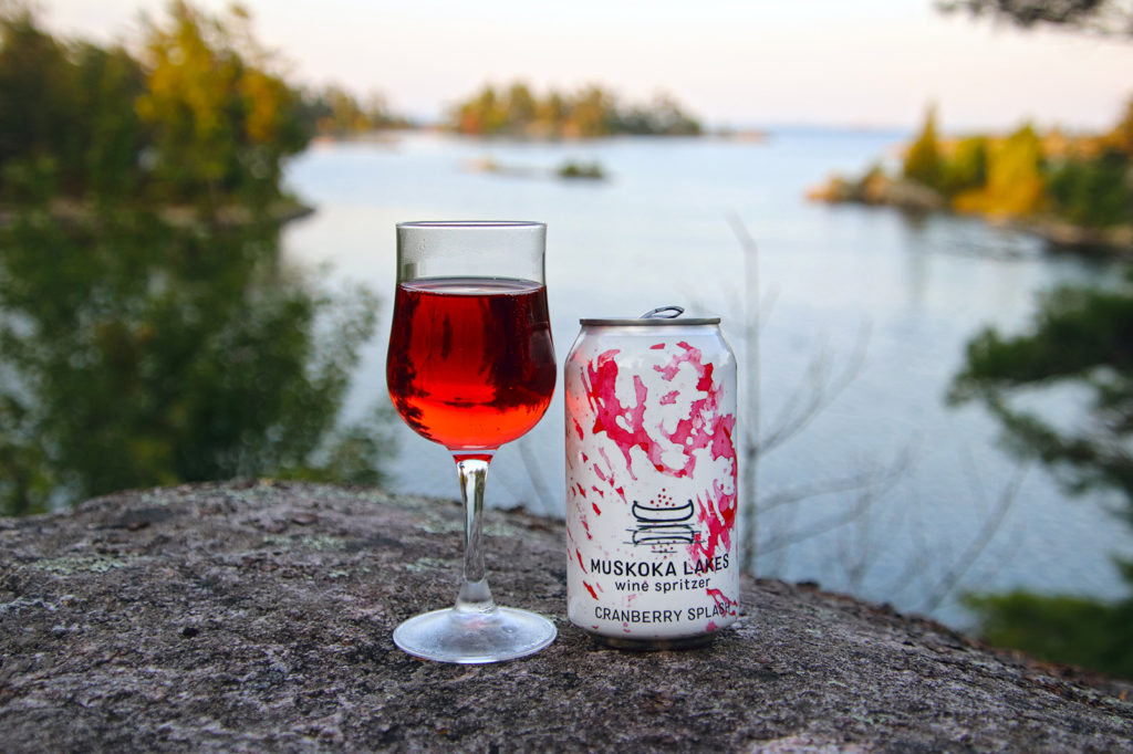 can and glass of cranberry splash wine spritzer on a rock overlooking a lake