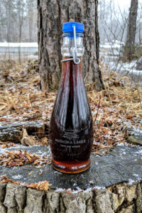bottle of maple syrup sitting on a tree stump