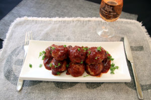 spicy turkey meatballs with cranberry glaze on a plate with a glass of wine