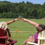 couple sitting in muskoka chairs outside toasting with wine glasses