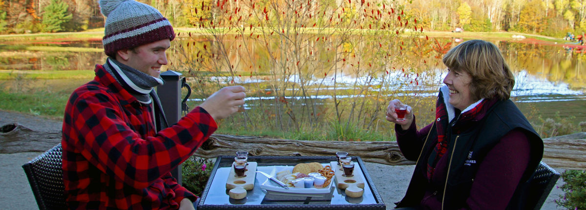 two people with wine and cheese on a patio with a view of water and trees