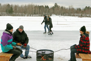 people in winter around a fire pit with skaters in the background