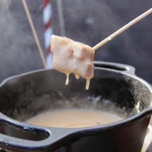 bread dripping with cheese above a pot of fondue