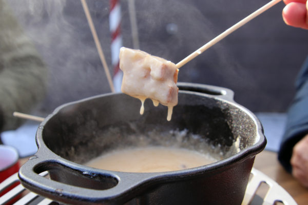 bread dripping with cheese above a pot of fondue