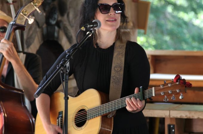 Christina Hutt playing her guitar while singing in a rustic setting