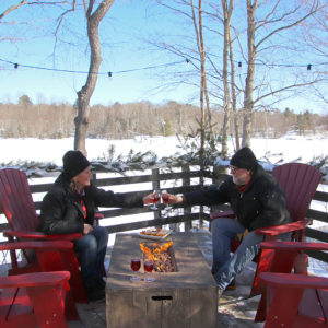 couple cheers with wine glasses at an outdoor fire table with muskoka chairs