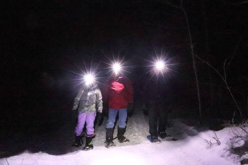 three people snowshoeing at night with headlamps